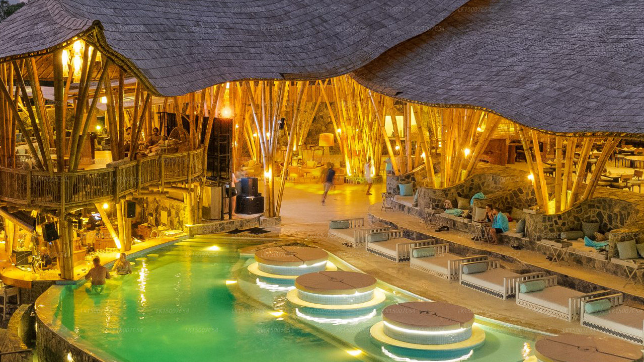 Bamboo-themed open-air restaurant with warm lighting and poolside seating at night.