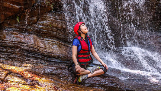 Person in a life jacket sitting on a rock with a waterfall in the background