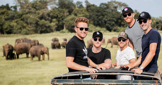 A group of people posing for a photo on a safari vehicle with elephants in the background.